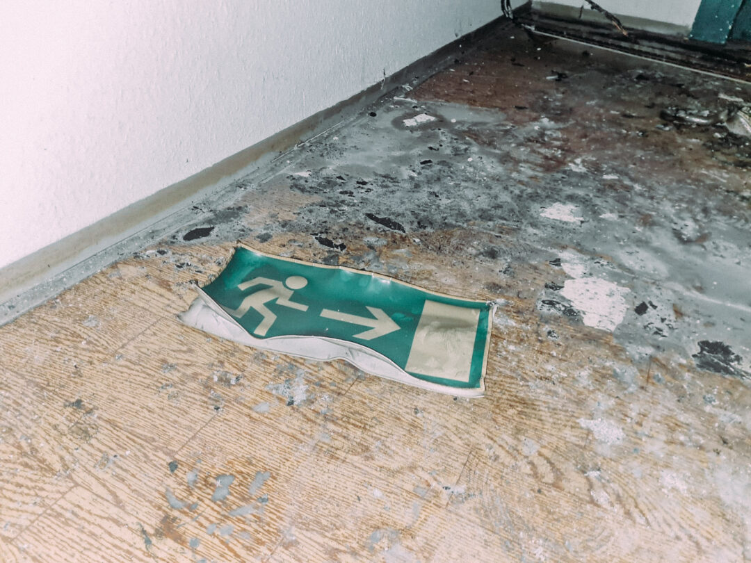 ein abgefallenes, grünes und eicht ineinandergeschmolzenes Fluchtwegsschild auf dem rußigen Fußboden