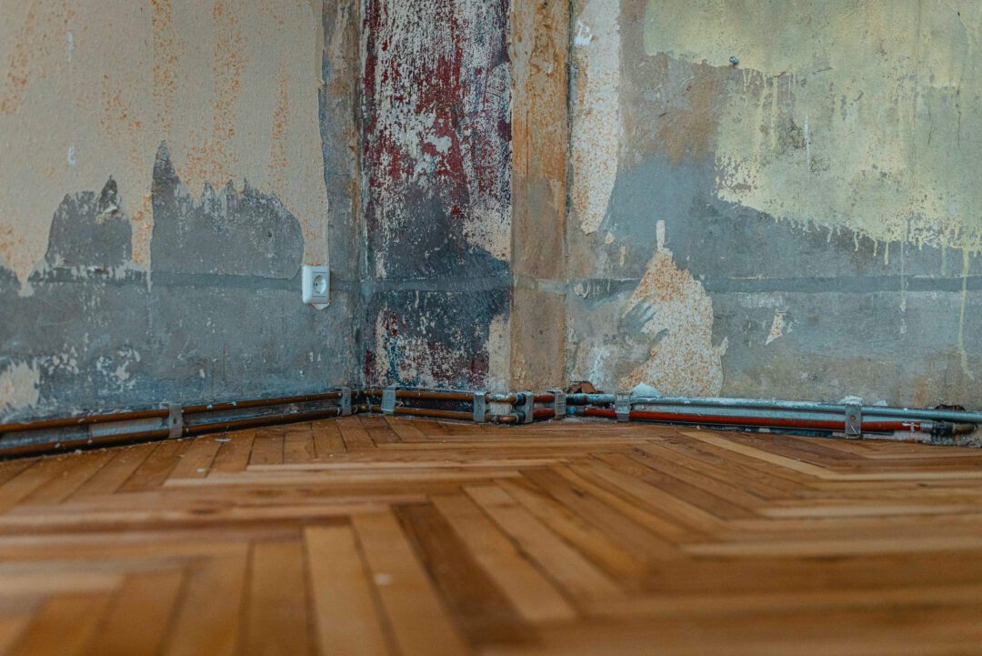 Detailaufnahme des Fischgrätenparketts und der Wand, von welcher die tapete abgerissen wurde