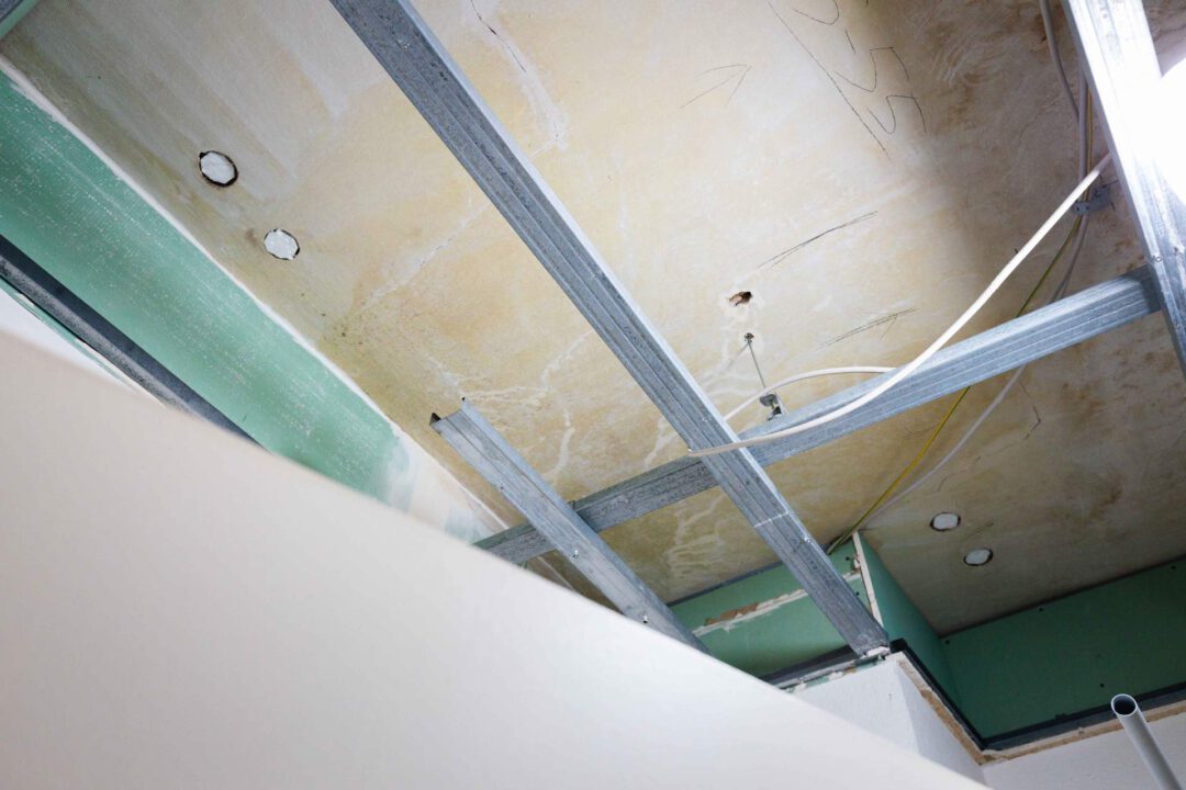 Blick auf die Deckenkonstruktion mit einer Metallunterkonstruktion für eine abgehängte Decke oder Trockenbau. Die Decke zeigt Spuren von Sanierungsarbeiten.