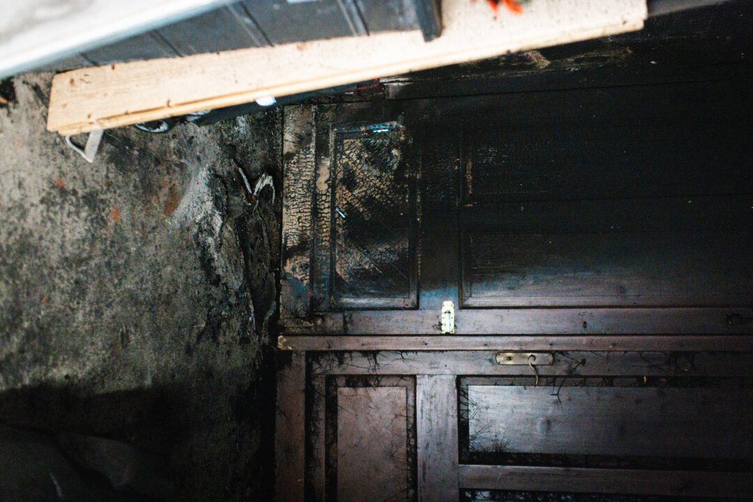 Detail der Zerstörung: Durch eine Explosion gesprengte und schwarz verkohlte Eingangstür nach Brandstiftung.