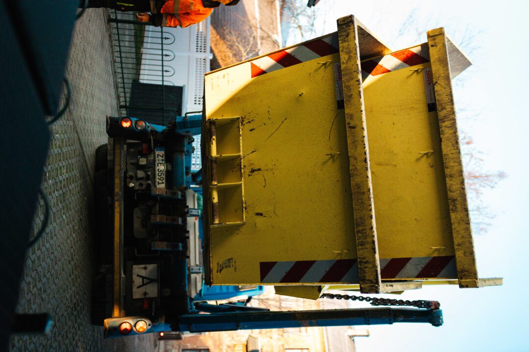 Abtransport von Brandgut: Ein großer gelber Schuttcontainer wird zur Entsorgung von zerstörtem Inventar verladen.