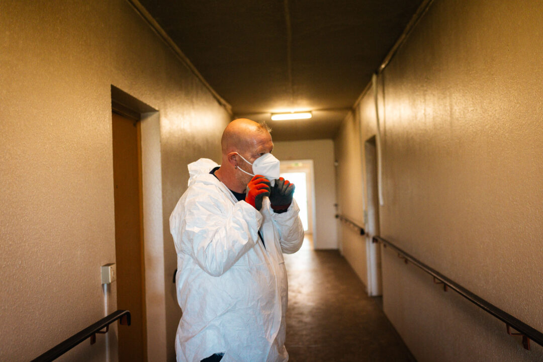 Mitarbeiter in Schutzanzug setzt seine Schutzmaske richtig auf