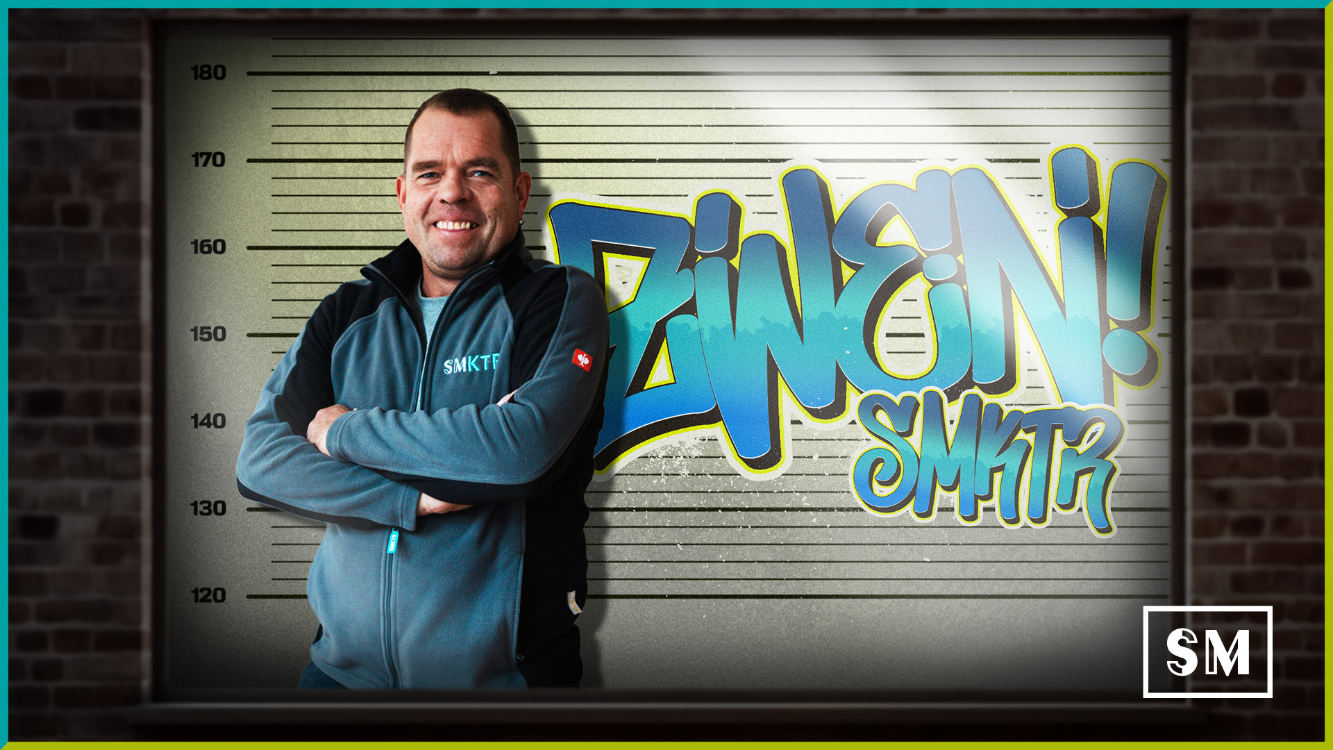 Lächelnder Mitarbeiter der Firma SMKTR in Arbeitskleidung vor einer Polizeifoto-Wand mit Graffiti-Schriftzug „Zwen!“ – Kreatives Mitarbeiterporträt im Crime-Style.