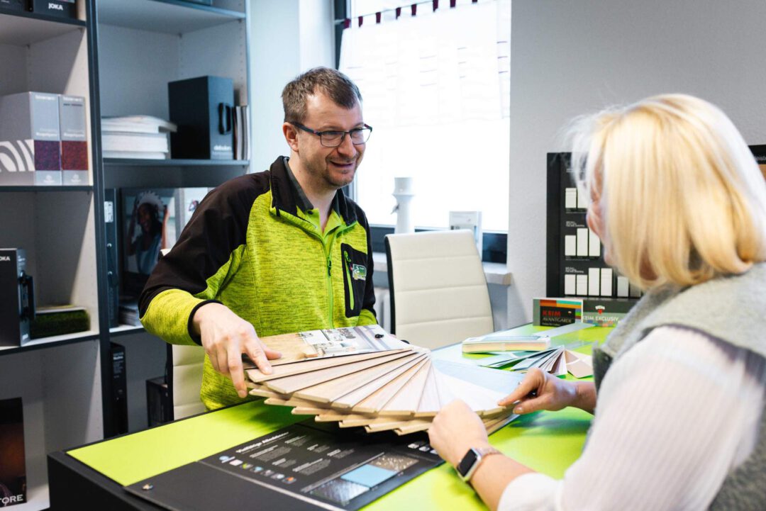 Kundenberatung auf Augenhöhe: zwei Mitarbeiter der Maler Palette GmbH bei der gemeinsamen Auswahl von Farbmustern und Bodenbelägen.
