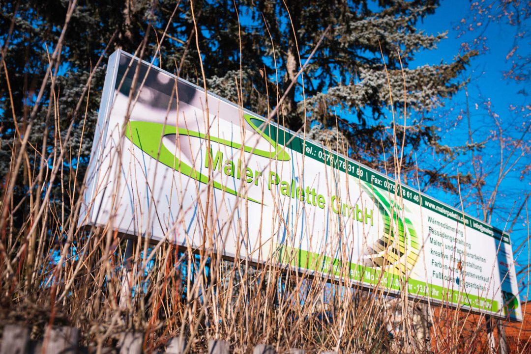 Werbebanner Maler Palette: Detailaufnahme des Firmenschilds der Maler Palette GmbH Zwickau zwischen Sträuchern im Außenbereich.