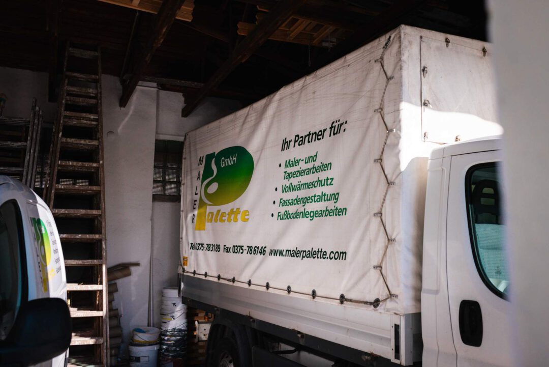 Service-LKW Maler Palette: Heckansicht eines Firmenfahrzeugs mit Leistungsübersicht: Malerarbeiten, Tapezierarbeiten, Vollwärmeschutz und Fußbodenlegearbeiten.