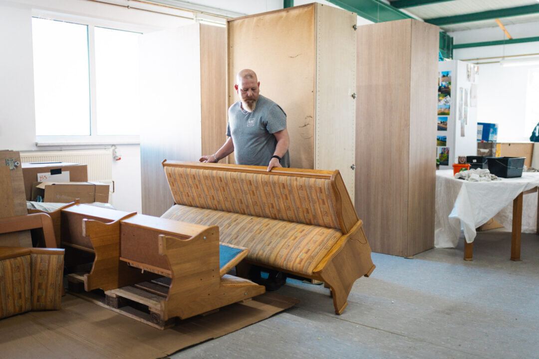 Facharbeiter Mike begutachtet eine gepolsterte Eckbank in der Sanierungshalle zur Einschätzung der Geruchsbeseitigung und Reinigung.