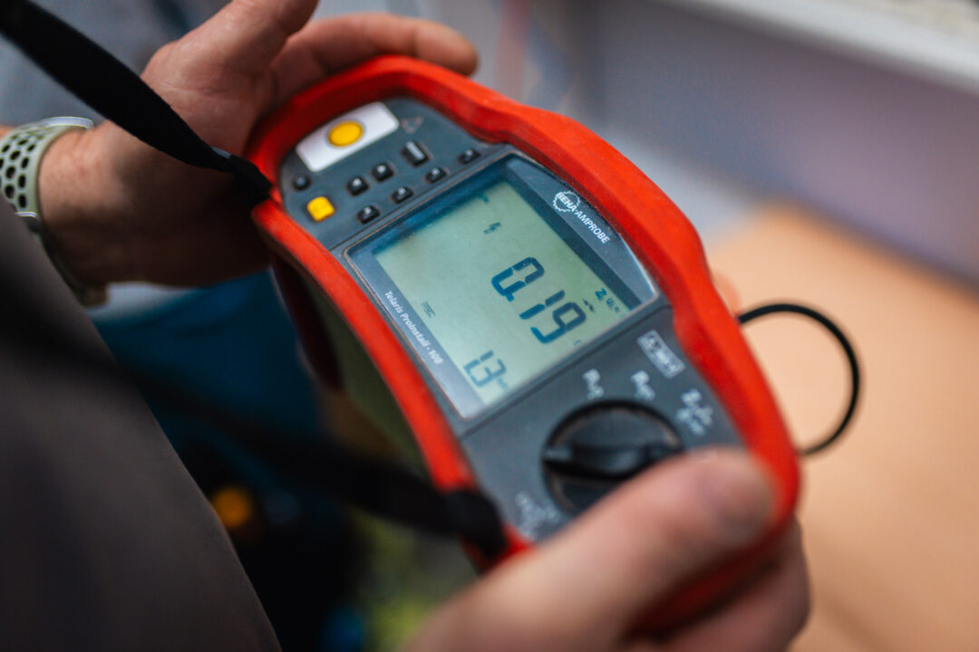 Nahaufnahme eines digitalen Beha-Amprobe Prüfgeräts bei der Messung von elektrischen Werten während einer Installation durch das Handwerker-Team.