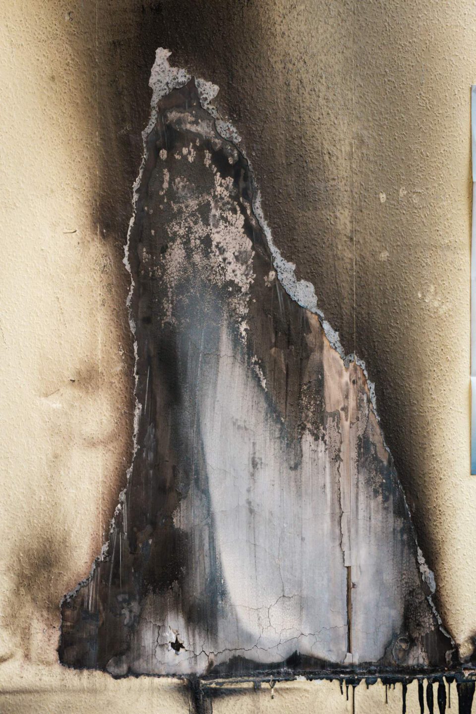 Nahaufnahme einer massiven Brandstelle an einer Wand mit abgeplatztem Putz und dicken Rußschichten vor der professionellen Schadenssanierung.