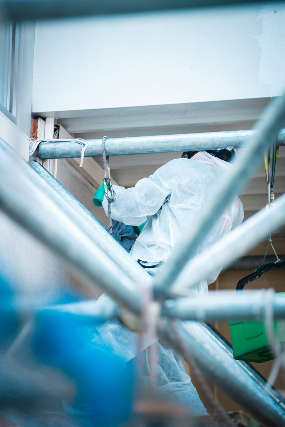 Professioneller Höhenarbeiter der Höhenservice Straß GmbH im weißen Schutzanzug und mit Sicherheitsseil bei der Rußbeseitigung an einer Dachkonstruktion nach einem Brandschaden.