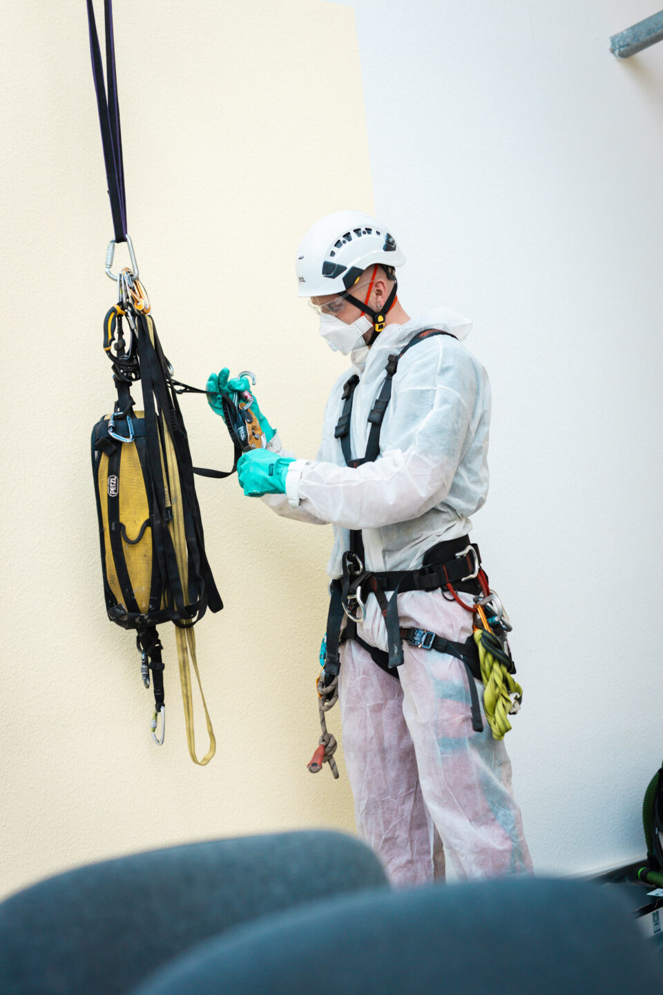Handwerker im Schutzanzug mit Atemschutzmaske, Schutzbrille und Helm legt die Kletterausrüstung und den Sicherheitsgurt für die Höhenarbeiten zur Brandschadensanierung an.