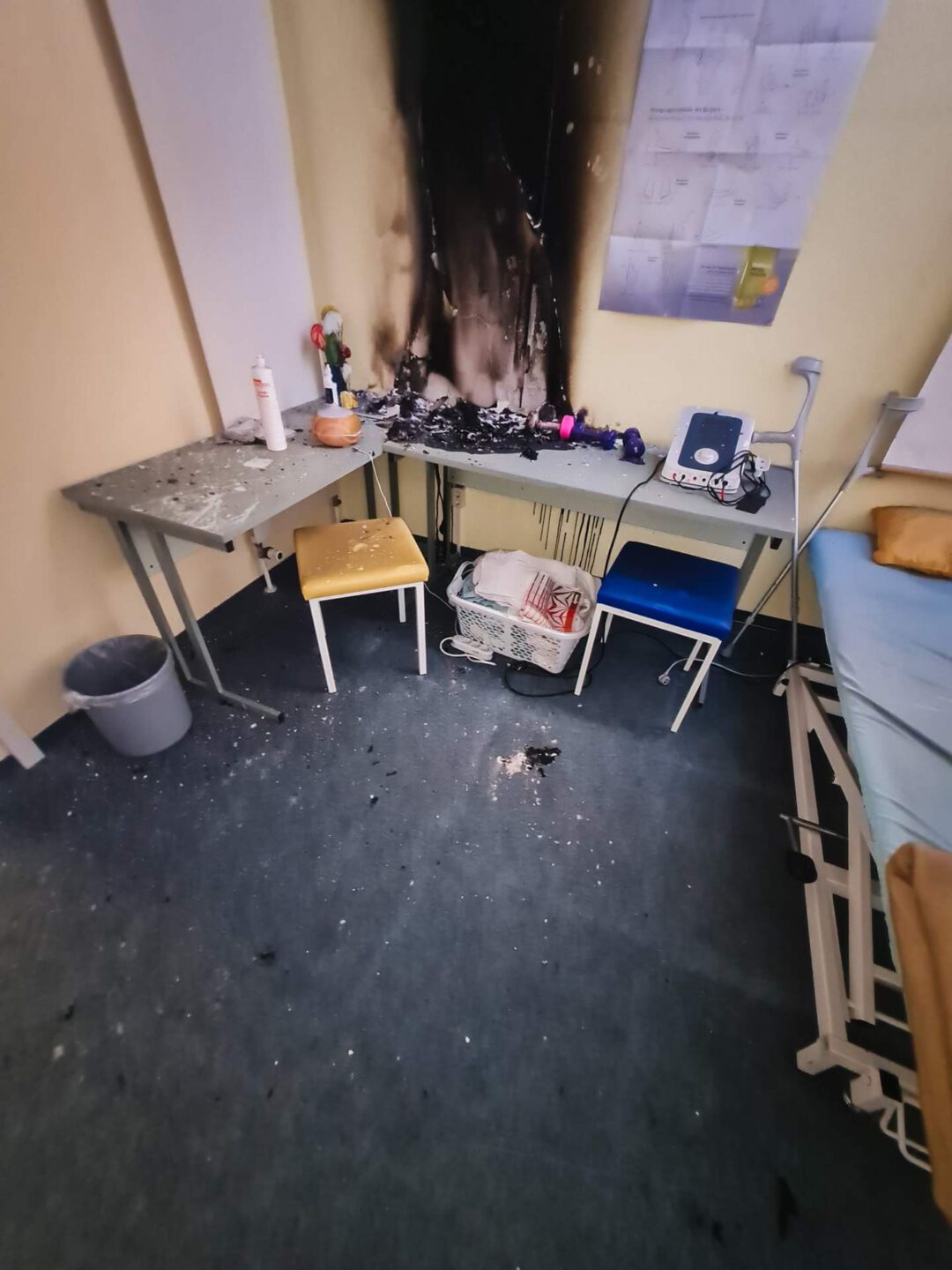 Der Ursprung des Brandschadens: Eine tiefschwarz verrußte Wand über einem Tisch in einem Physiotherapie-Klassenzimmer mit Brandrückständen auf den Möbeln vor der Sanierung.